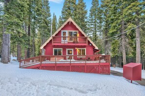 A red cabin with a balcony, surrounded by trees and snow.