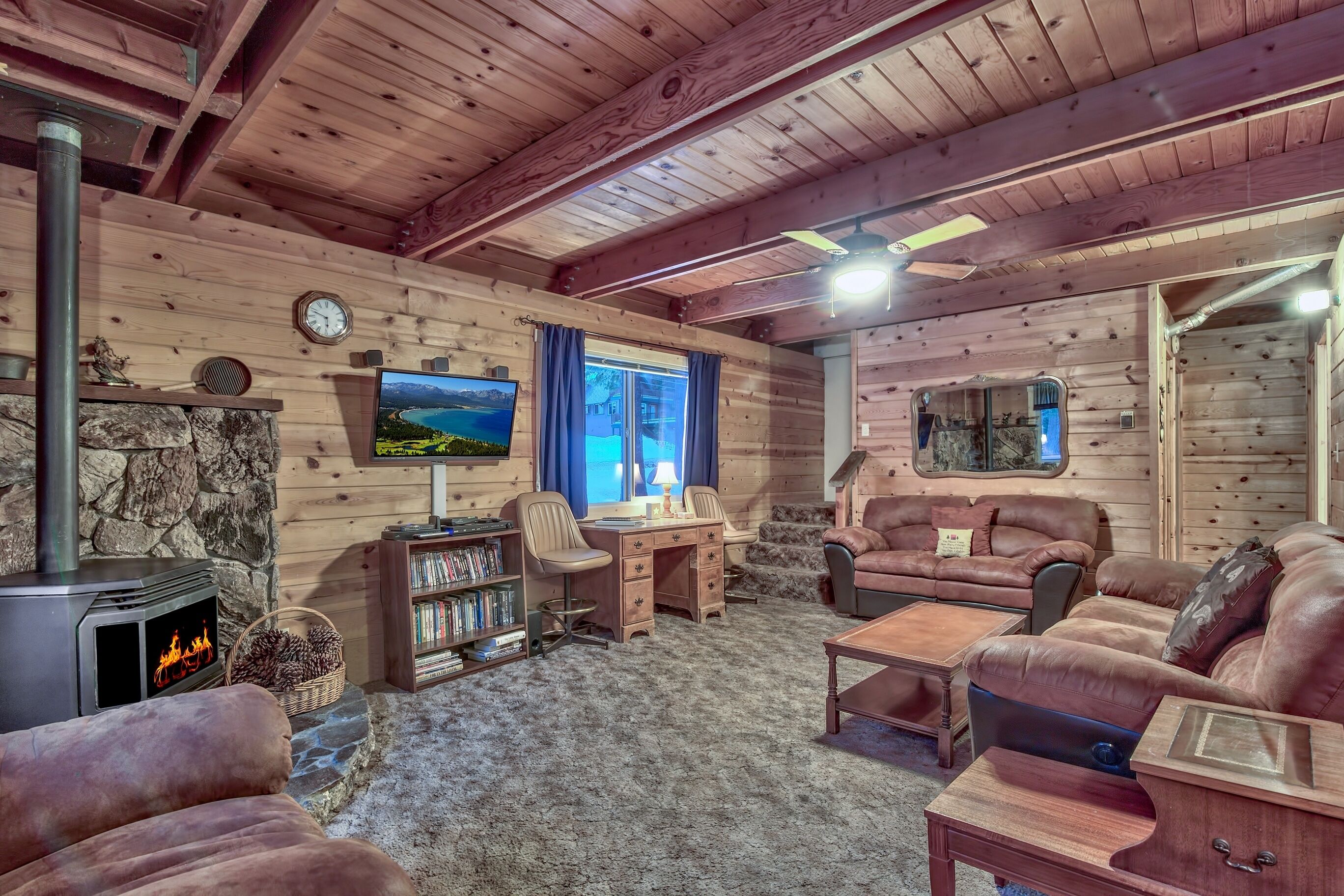L’intérieur chaleureux d’un chalet avec une cheminée en pierre, des meubles en cuir, un téléviseur et une grande fenêtre.