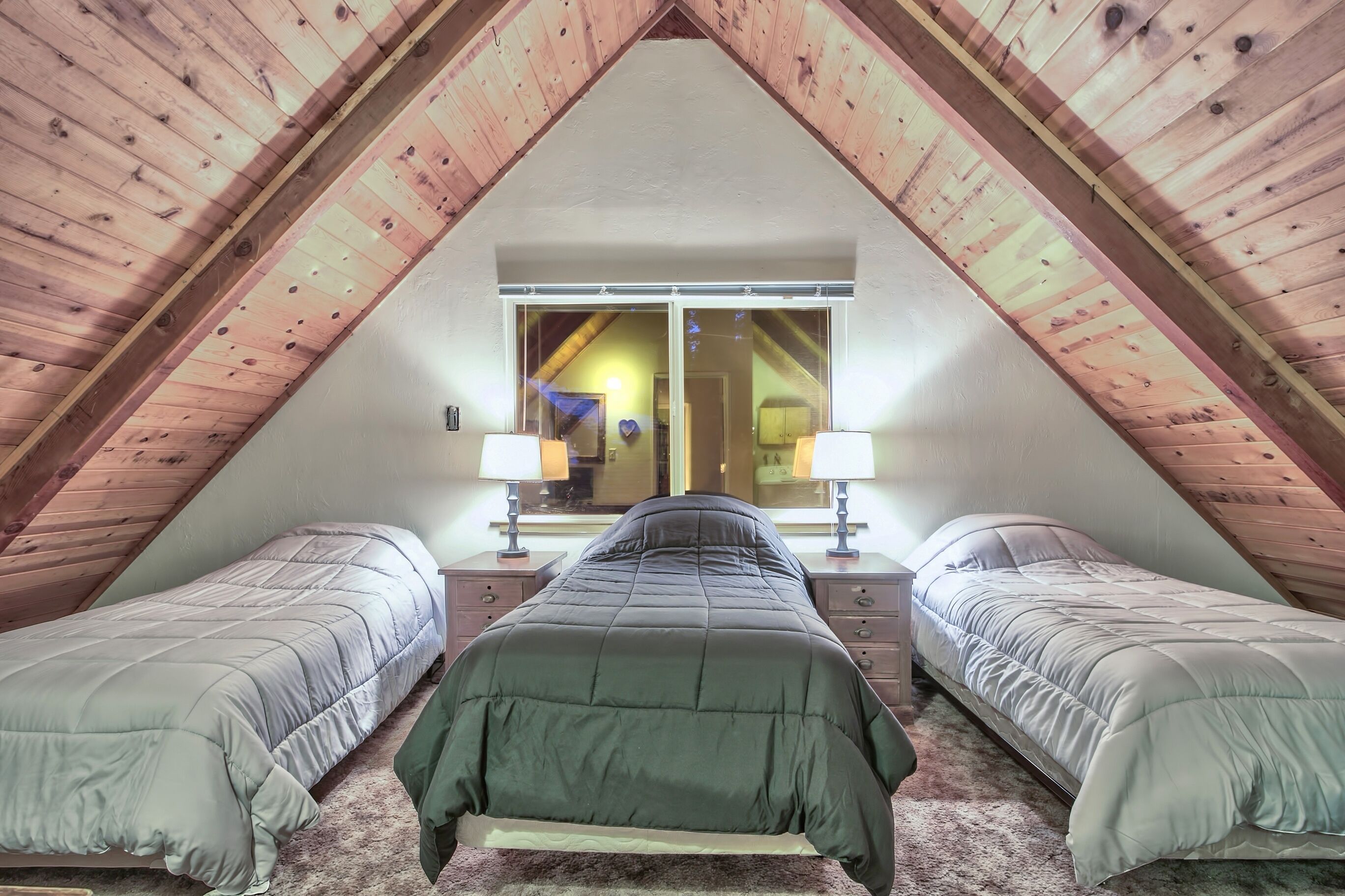 Une chambre avec deux lits simples, une grande fenêtre et des poutres en bois au plafond.
