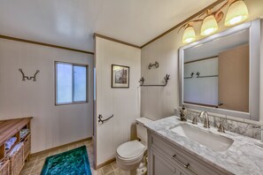 A bathroom with a white toilet, a sink with a marble countertop, a large mirror, and a window.