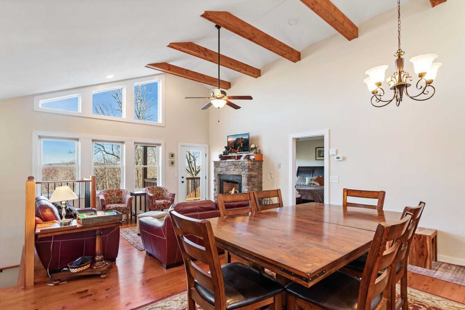 A spacious dining area with a large wooden table and chairs, a chandelier, and a fireplace.