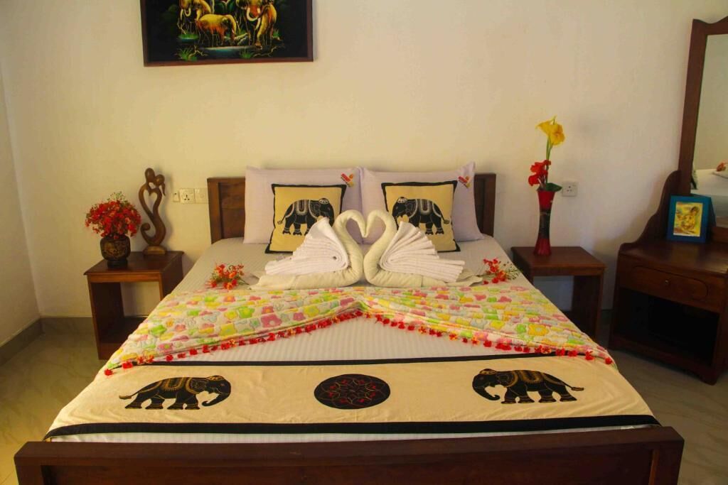 Una cama bien hecha con un edredón colorido, dos almohadas con diseños de elefantes y una disposición de toallas con forma de corazón.