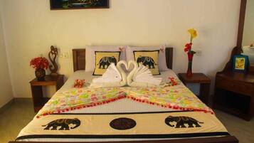 Una cama bien hecha con un edredón colorido, dos almohadas con diseños de elefantes y una disposición de toallas con forma de corazón.