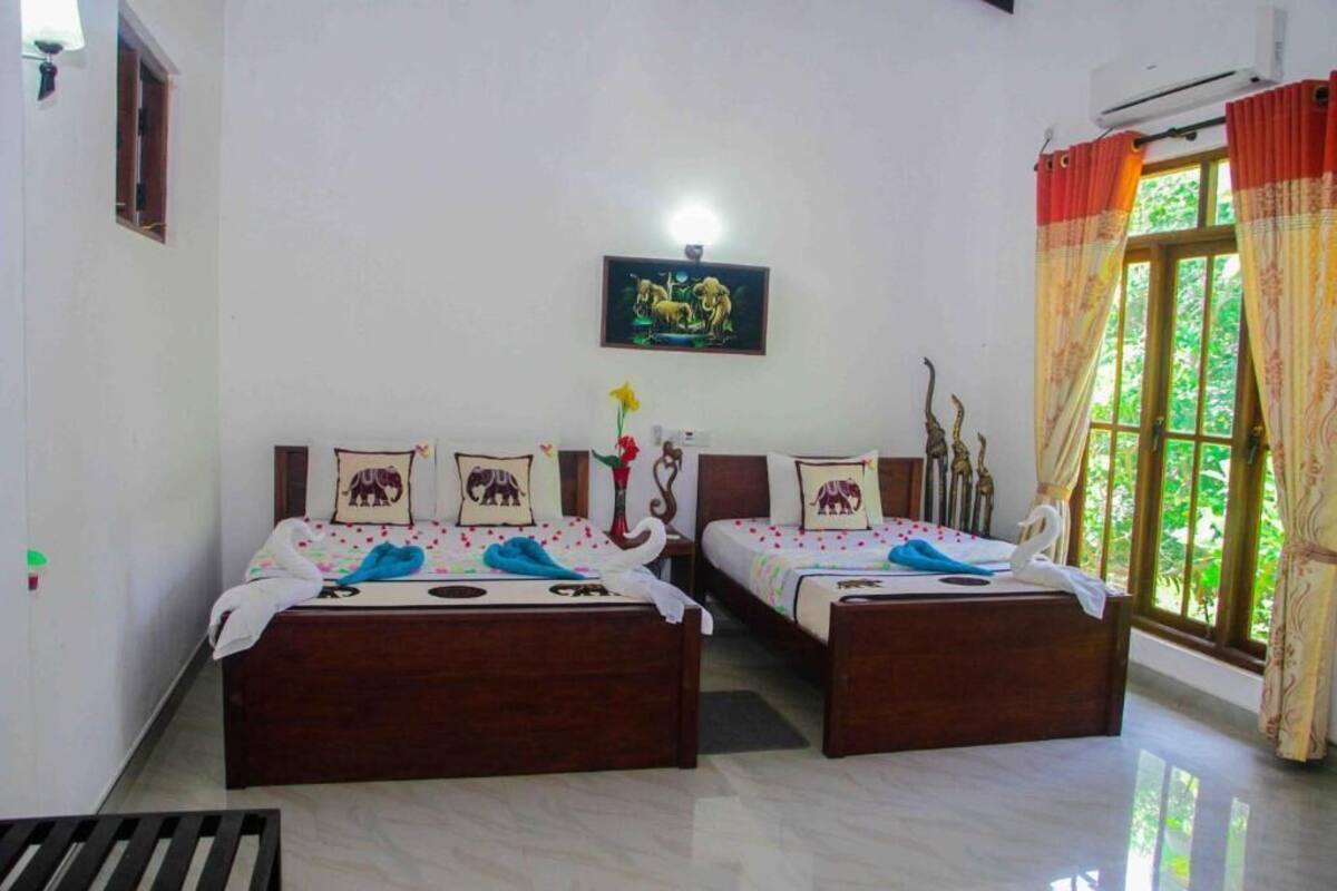 A room with two wooden beds, a small table, a wall-mounted picture, and a window with curtains.