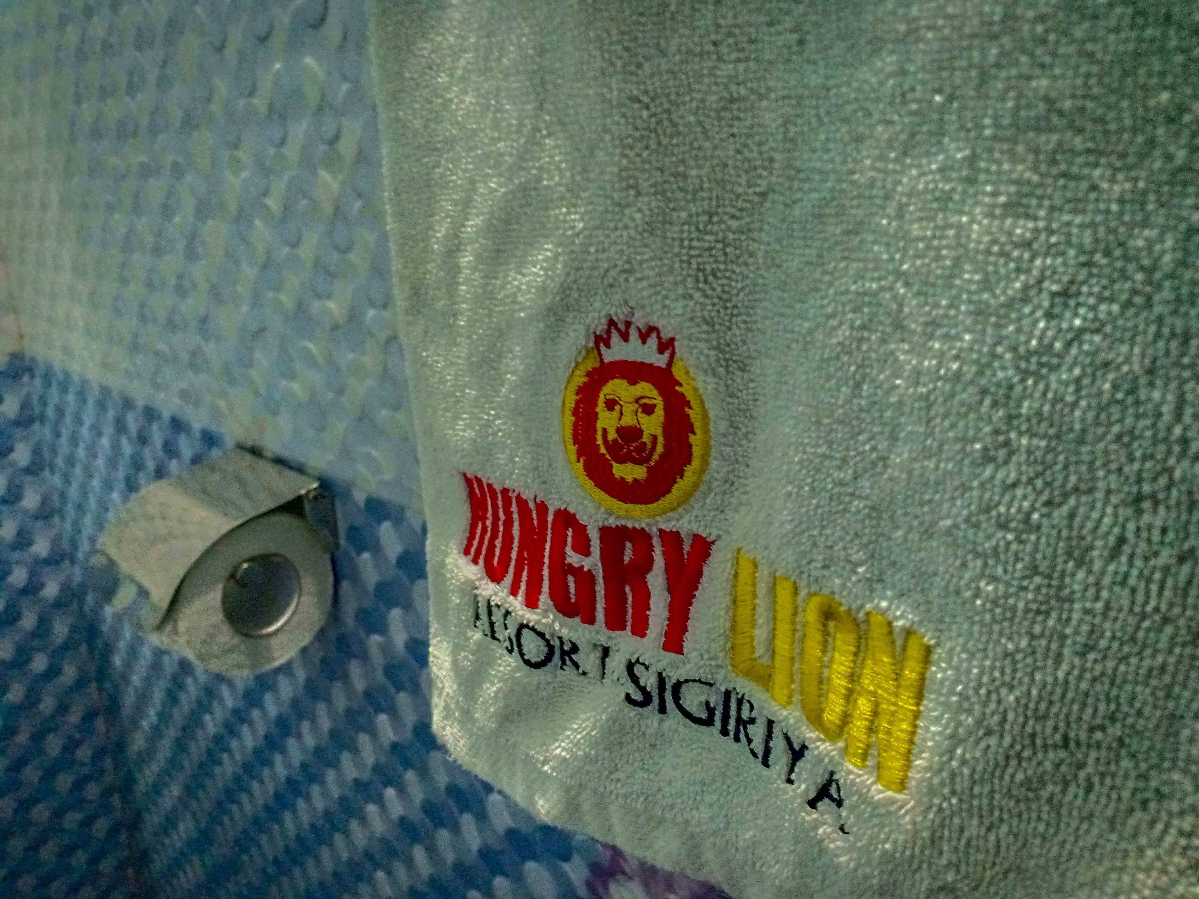 A close-up of a fabric with embroidered text and a lion's head logo, likely part of a hotel's interior decor.