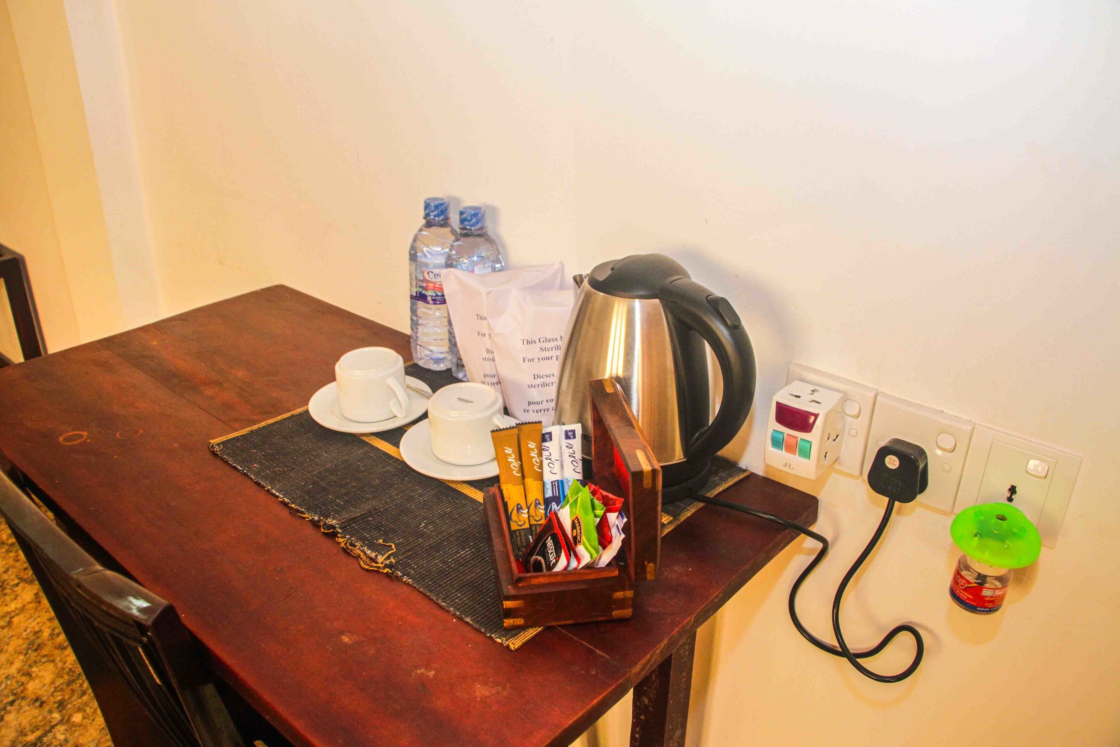 A wooden table with a coffee pot, water bottles, a tissue box, and a tissue dispenser.