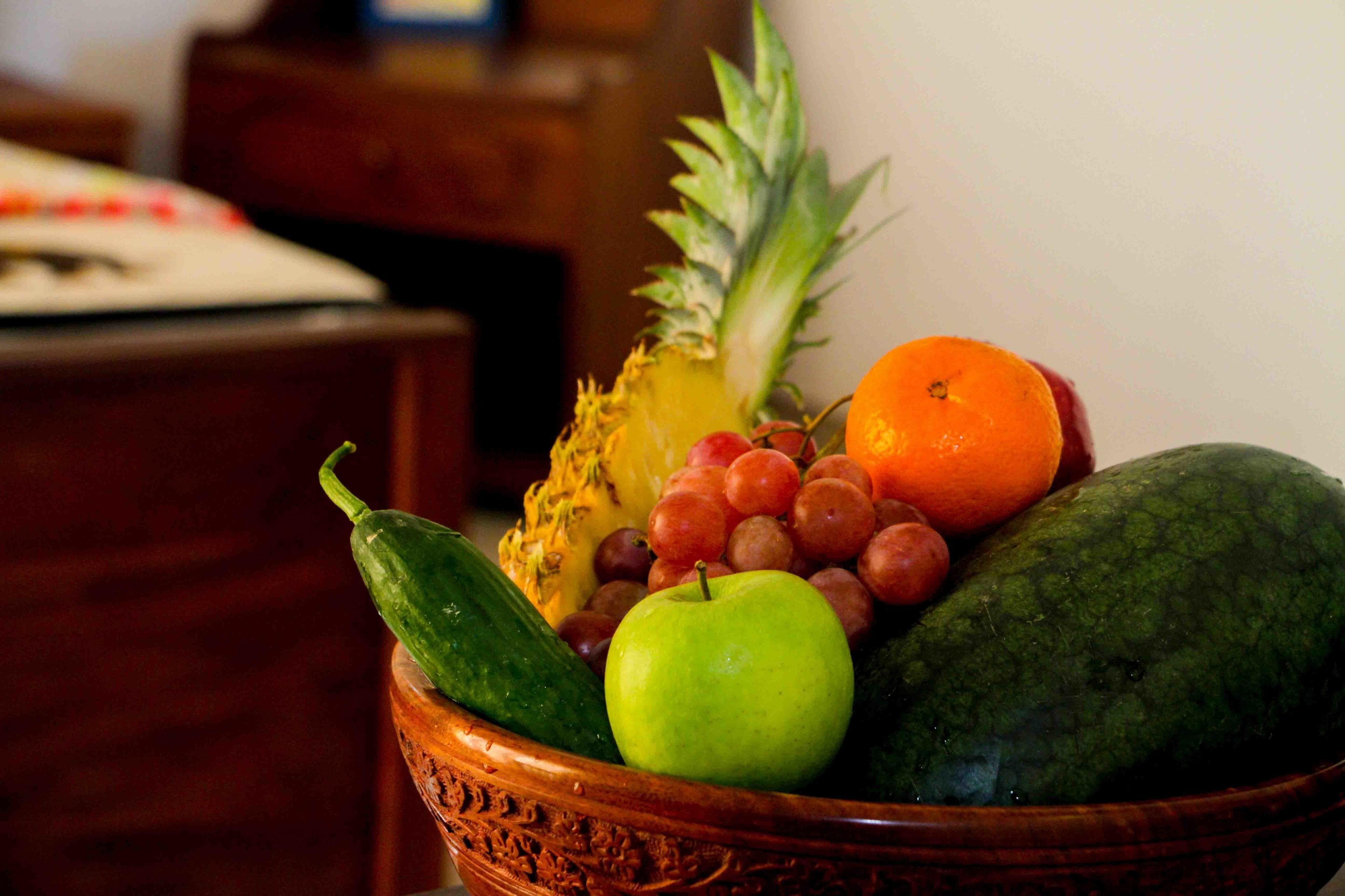 Un tazón de madera con piña, manzana, uvas, naranja y pepino.
