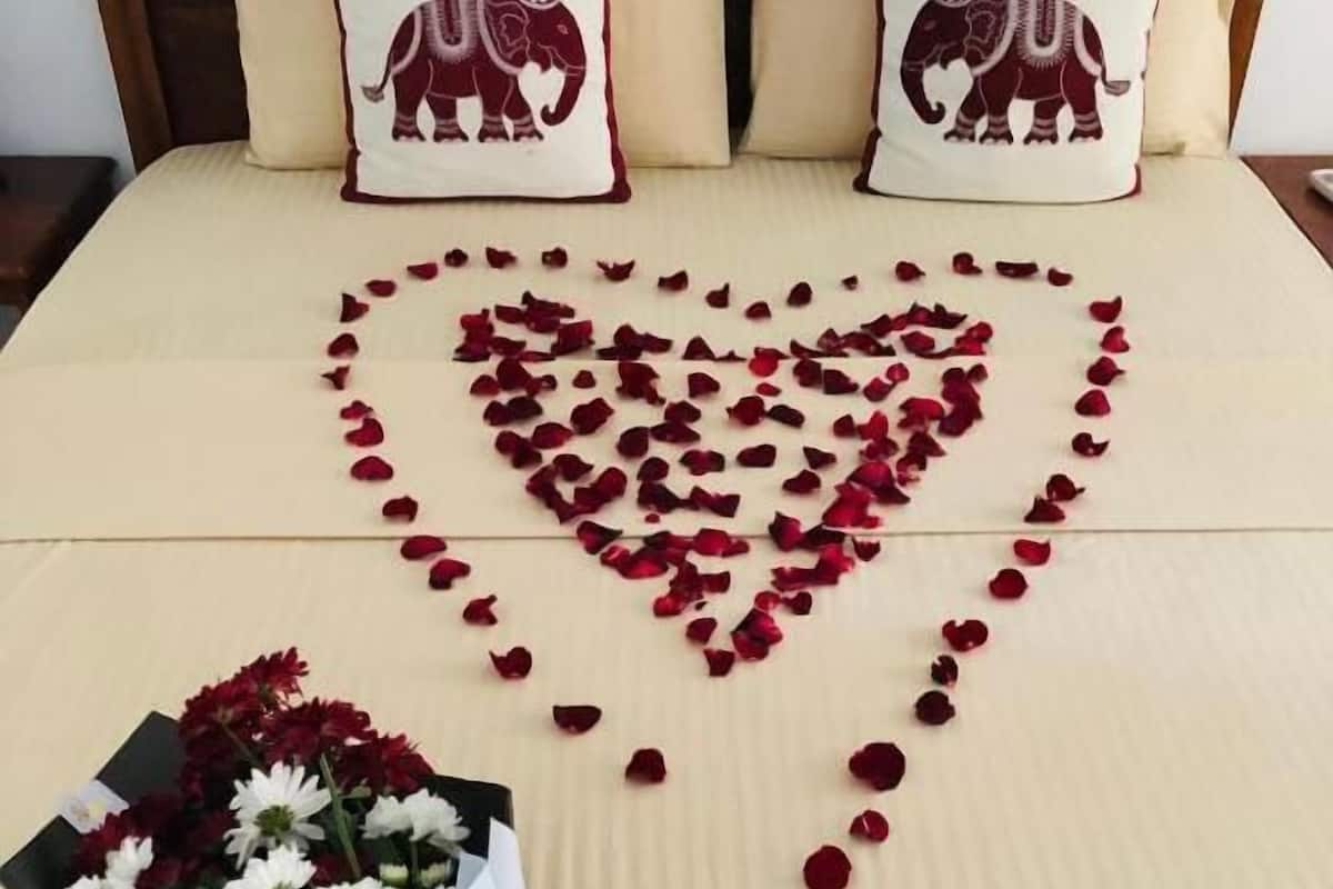 A bed with a heart-shaped arrangement of rose petals and a bouquet of flowers.