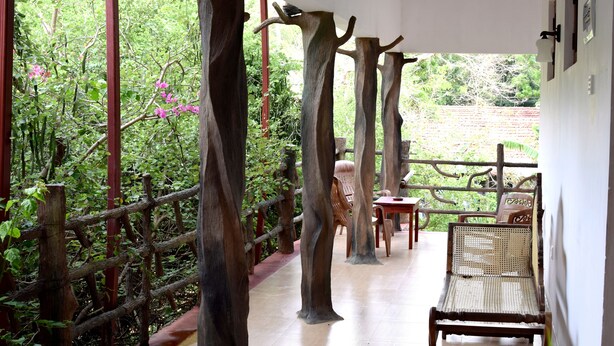A covered outdoor seating area with wooden tree-like columns, a bench, and a table. - Hungry Lion Sigiriya (Sigiriya)