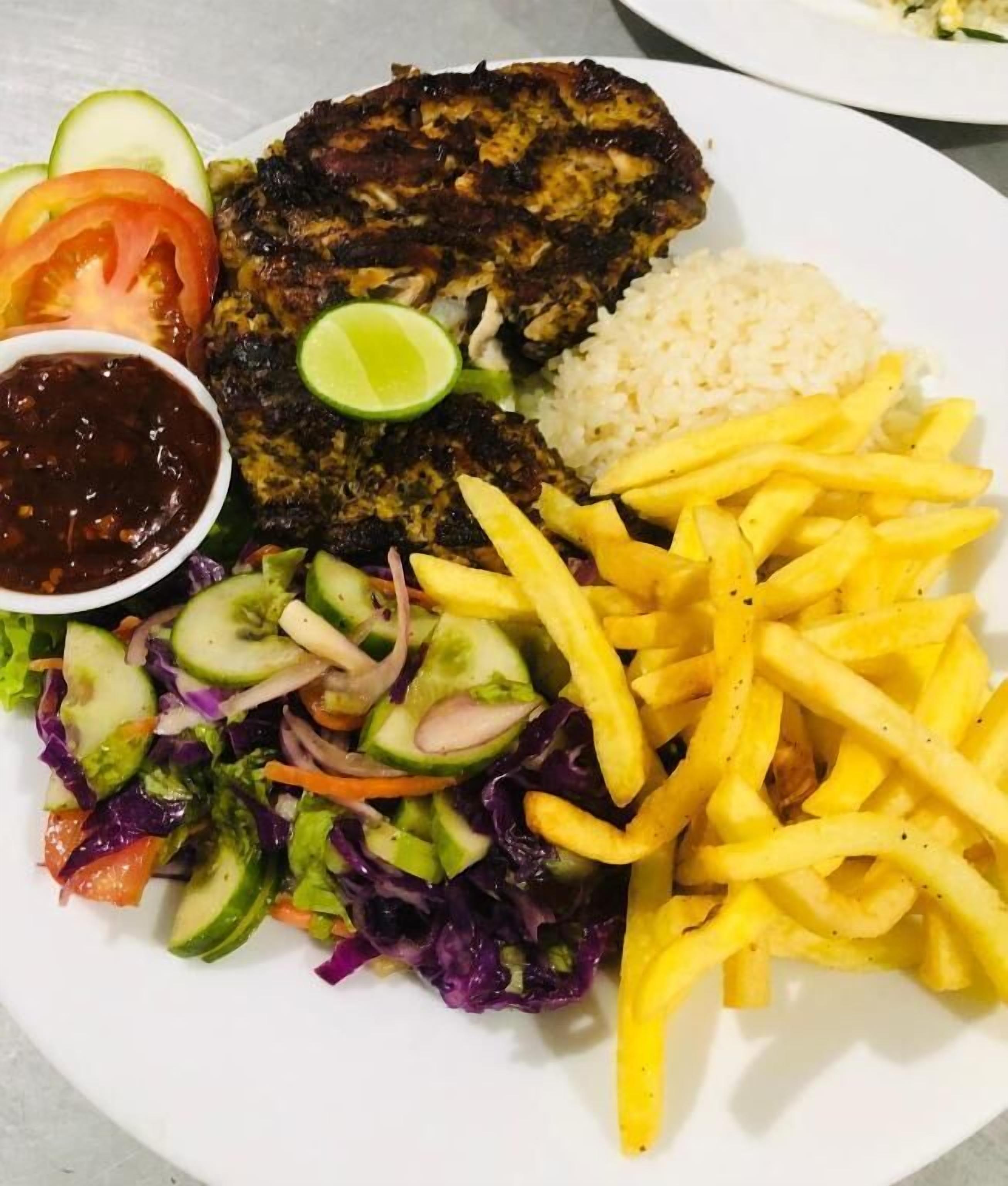 A plate with a grilled meat, rice, French fries, a salad, and a side of sauce.