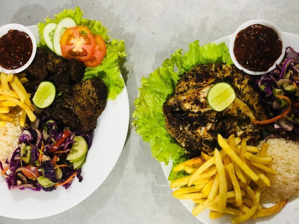 Two plates of food with meat, fries, rice, and salad.