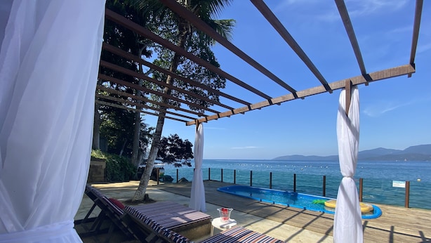 A poolside area with a pergola, lounge chairs, and a view of the sea. - Pousada Serra e Mar (Angra dos Reis)