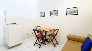 Ein kompakter Wohnbereich mit Küchenzeile, einem Esstisch mit Stühlen, einer Couch und drei gerahmten Bildern an der Wand.