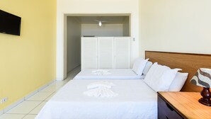 Ein Hotelzimmer mit zwei Betten, einem flachbildfernseher an der Wand, einem Deckenventilator und einem Nachttisch aus Holz mit einer Lampe.