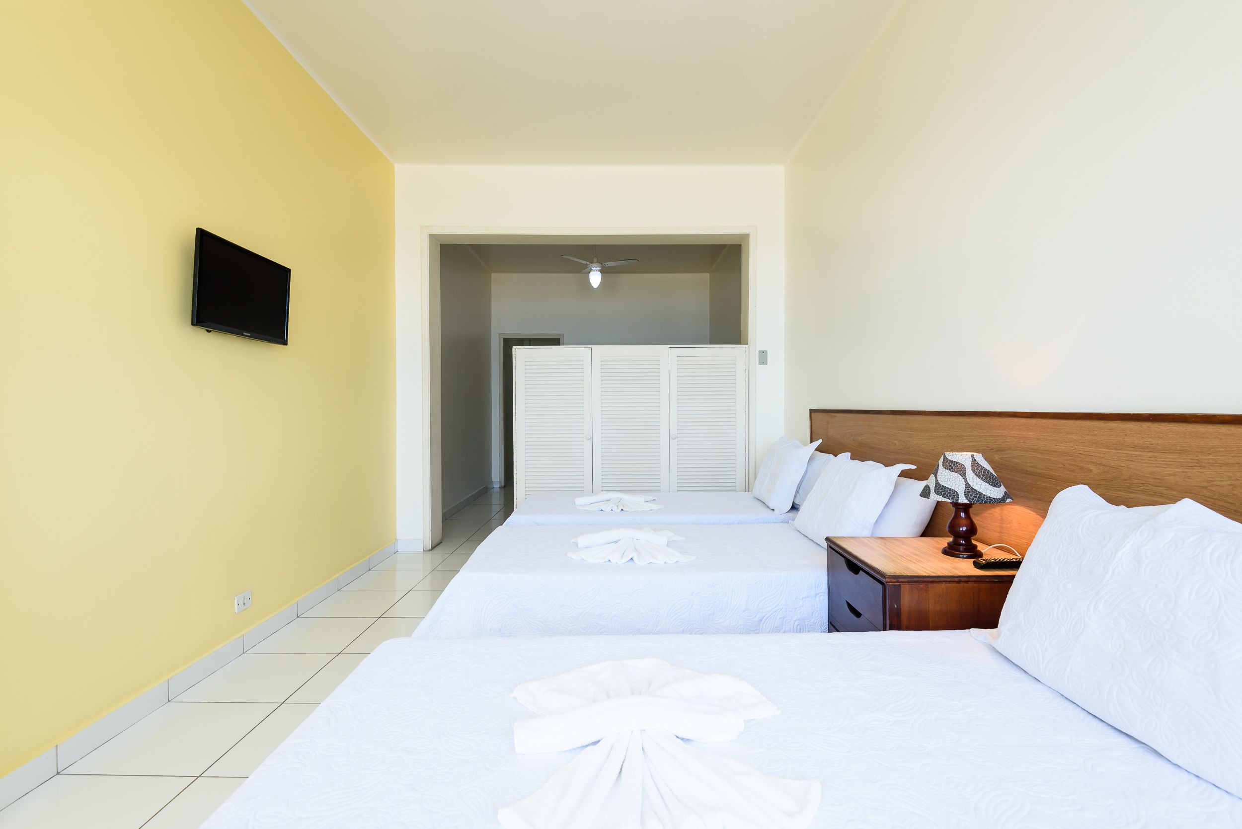 A hotel room with two beds, a television, a ceiling fan, and a nightstand with a lamp.