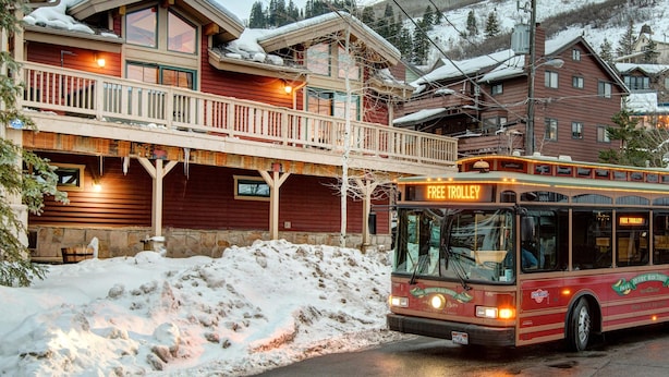 Un autobus rouge portant l’inscription « Navette gratuite », garé devant un bâtiment en bois doté d’un balcon et dont le toit est recouvert de neige.