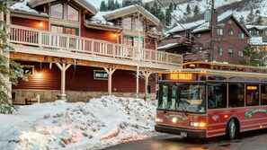 A red bus with "Free Trolley" signage, parked in front of a wooden building with a balcony and snow on the roof. - Main Street Lookout 3 Bedroom Townhouse by RedAwning (Park City)
