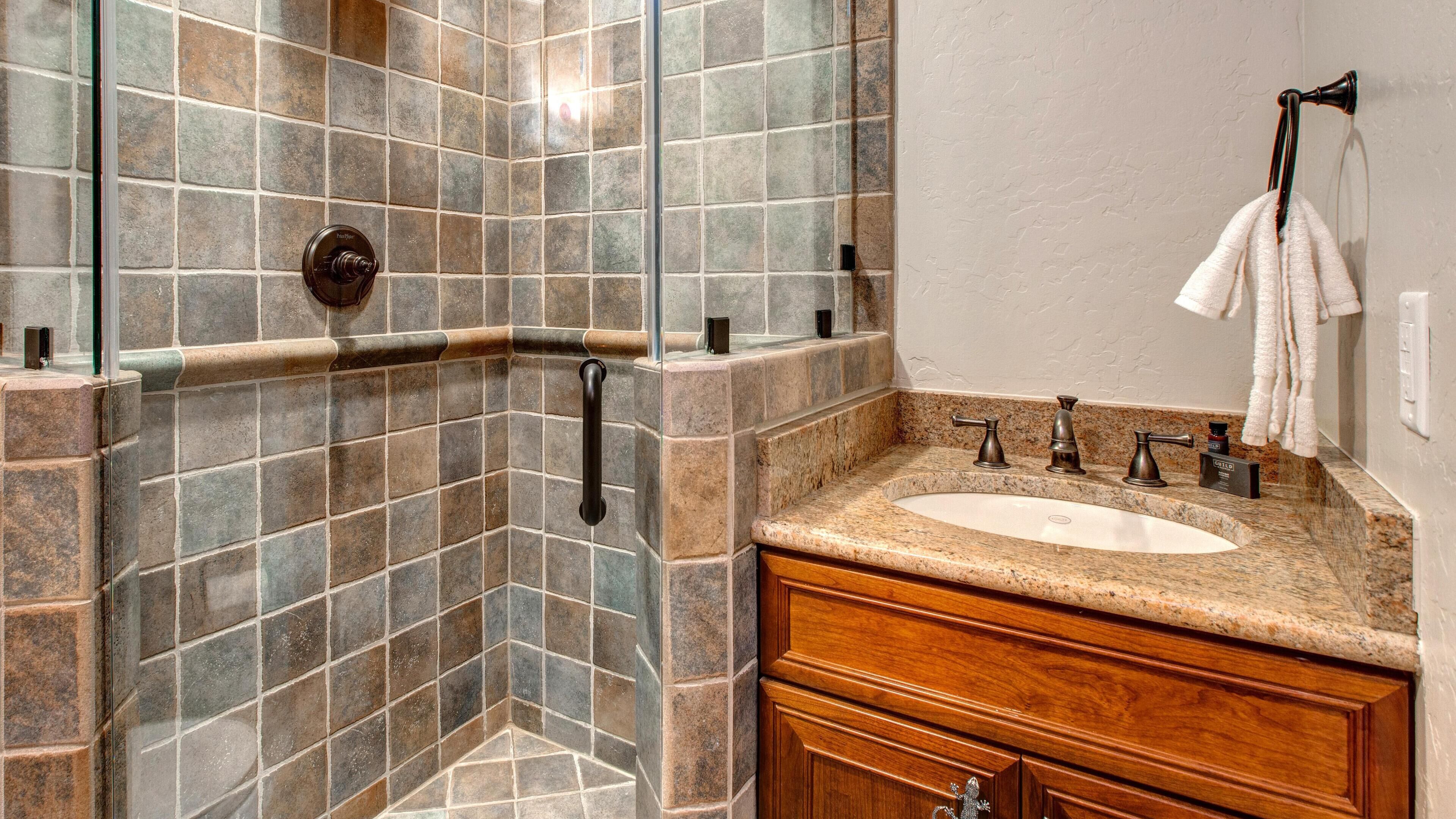 A bathroom with a glass shower enclosure, a granite countertop sink, and wooden cabinetry.
