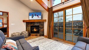 Un salon chaleureux avec une cheminée, des sièges confortables et une grande fenêtre donnant sur l’extérieur.