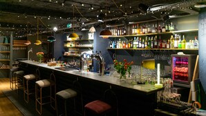 Un espace bar avec des tabourets, un comptoir, des étagères remplies de bouteilles et un panneau lumineux au néon.