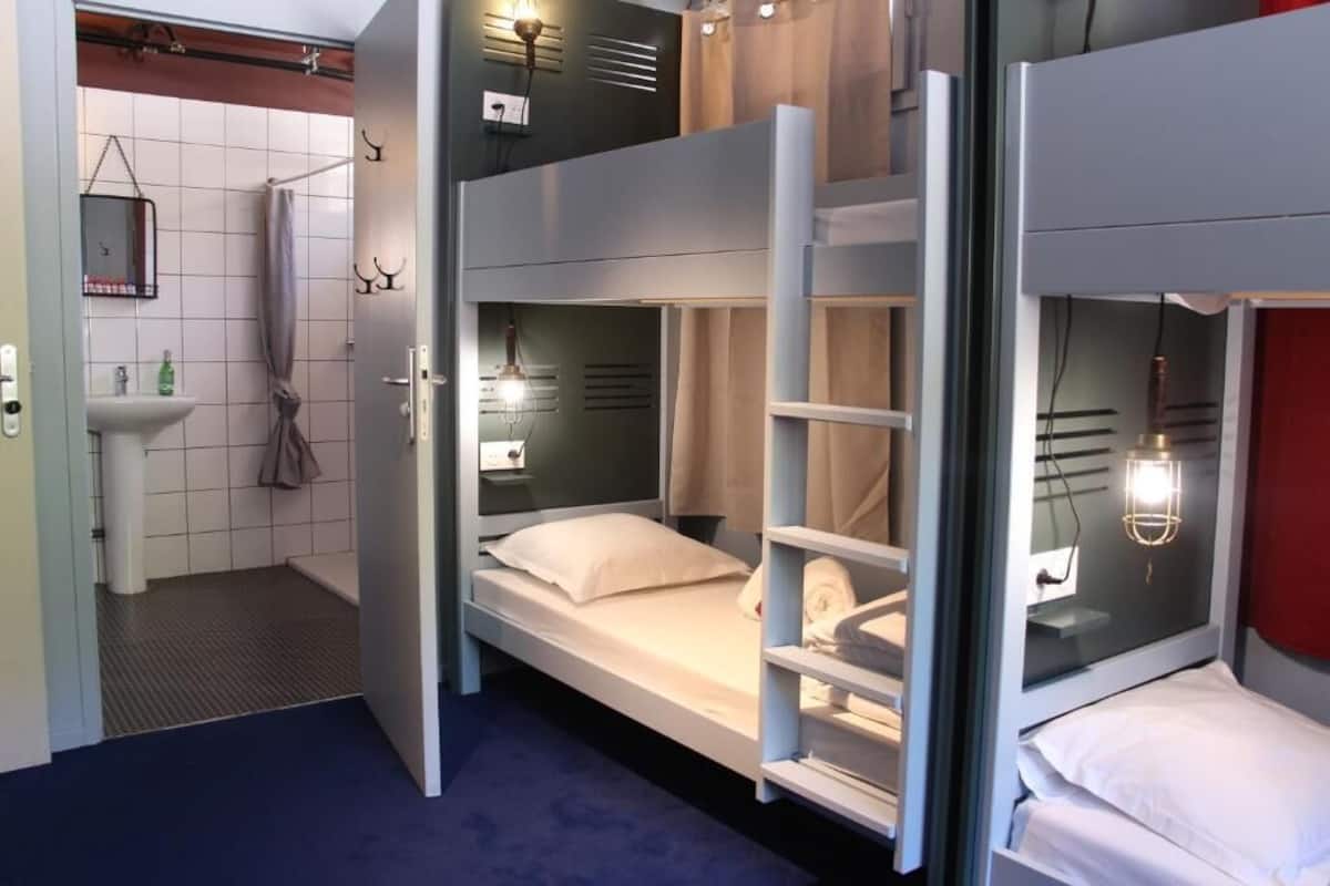 Une chambre d’hôtel compacte avec des lits superposés, une petite salle de bain avec un lavabo et un miroir.
