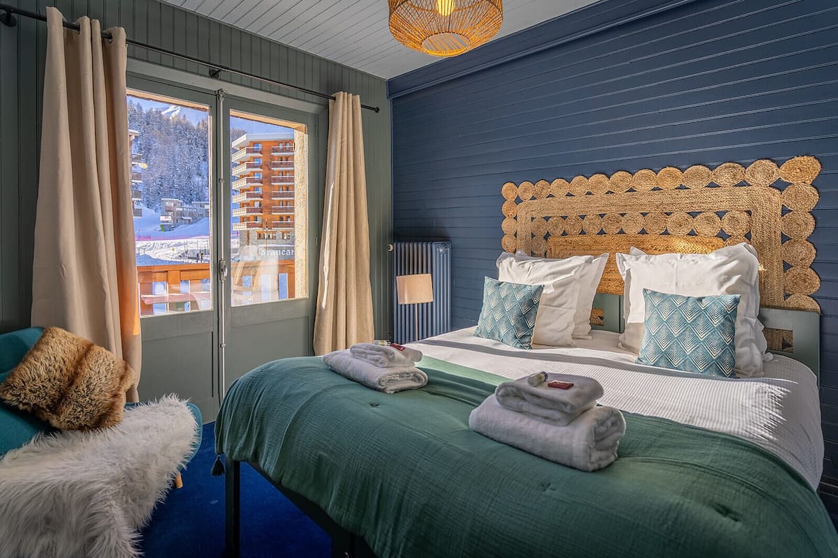 Une chambre d’hôtel avec un lit, une vue sur une montagne enneigée et une fenêtre avec des rideaux.