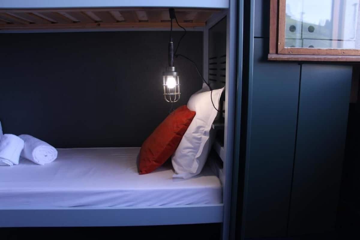 Un lit superposé avec un seul oreiller rouge, un oreiller blanc et des serviettes enroulées sur le lit du bas.