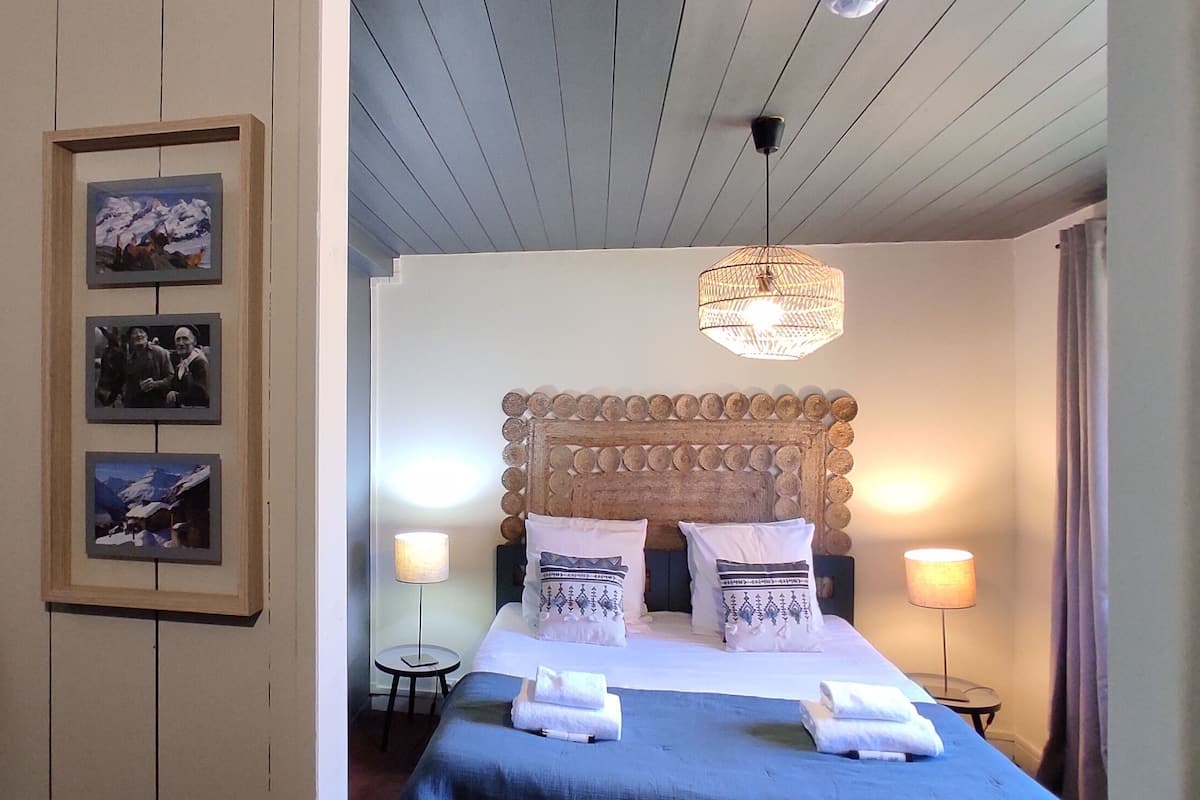Une chambre avec un lit, une tête de lit en bois et un porte-objets fixé au mur, sur lequel est posé un sac en tissu tressé.