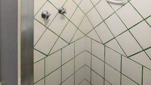 A bathroom with a white tiled wall featuring a diamond pattern and a shower area with a handheld showerhead. - Omar do Rio - Apartamento A802 (Rio de Janeiro)