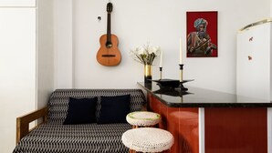Un salon moderne avec un canapé à motifs, une guitare, un tableau et un coin bar avec des tabourets.