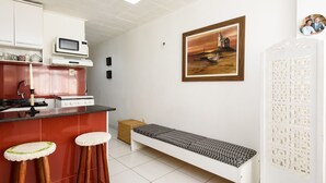 Une cuisine compacte équipée d’un four à micro-ondes, d’une cuisinière et de quelques tabourets. On peut également apercevoir un banc et un tableau encadré.