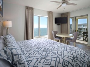 A hotel room with a large bed, a ceiling fan, a TV, a balcony with a table and chairs, and a view of the ocean. - Royale Palms 2307 (Myrtle Beach)