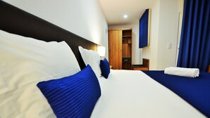 Habitación de hotel con dos camas, un armario de madera, un escritorio y un baño.
