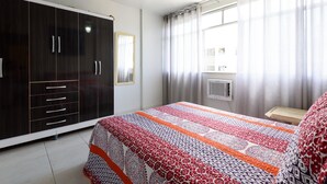 Une chambre à coucher comprenant un lit, une armoire, un ventilateur de plafond, une fenêtre avec des rideaux et un appareil de climatisation.