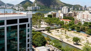 Une vue urbaine avec une montagne imposante en arrière-plan, une rivière qui traverse le centre-ville et divers bâtiments, dont un immeuble moderne en verre au premier plan.
