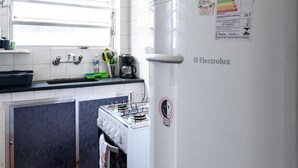 Une cuisine avec des meubles blancs, une cuisinière, un réfrigérateur et une fenêtre avec des stores.
