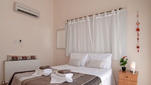 A hotel room with a bed, a bedside table with a lamp, a radiator, and a wall-mounted air conditioner. - Villa Puccini (Pegeia)