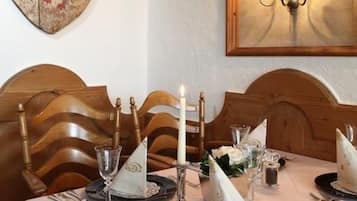 A dining table set with candles, napkins, and cutlery, with a shield-shaped wall decoration and a wall-mounted candelabra.