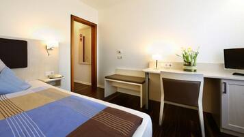 Ein Hotelzimmer mit Bett, Schreibtisch, Stuhl, Fernseher und einem kleinen Tisch mit Pflanze.