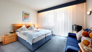Ein Hotelzimmer mit Bett, Sofa, Fernseher und einer Obstschale.