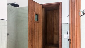 Une porte en bois avec une petite fenêtre, un espace douche aux carreaux verts et un mur recouvert de carreaux blancs.