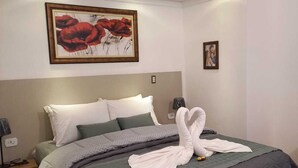 A neatly made bed with a swan towel design, a painting of red flowers, and a framed picture on the wall. - Hotel Casarão da Ducha (Campos do Jordão)
