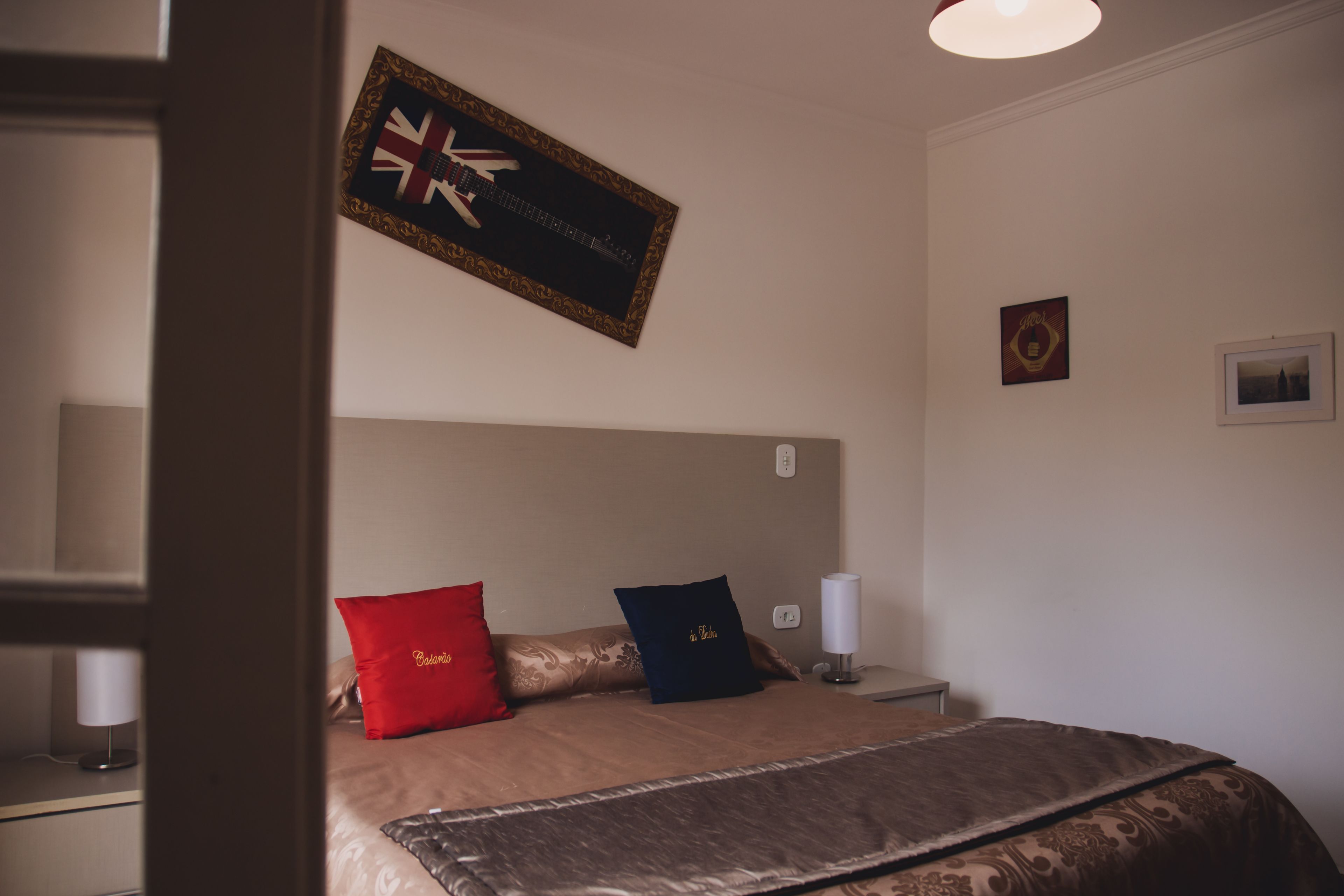 Un letto ben rifatto con una testiera, due cuscini, una lampada da comodino e un quadro incorniciato appeso al muro.