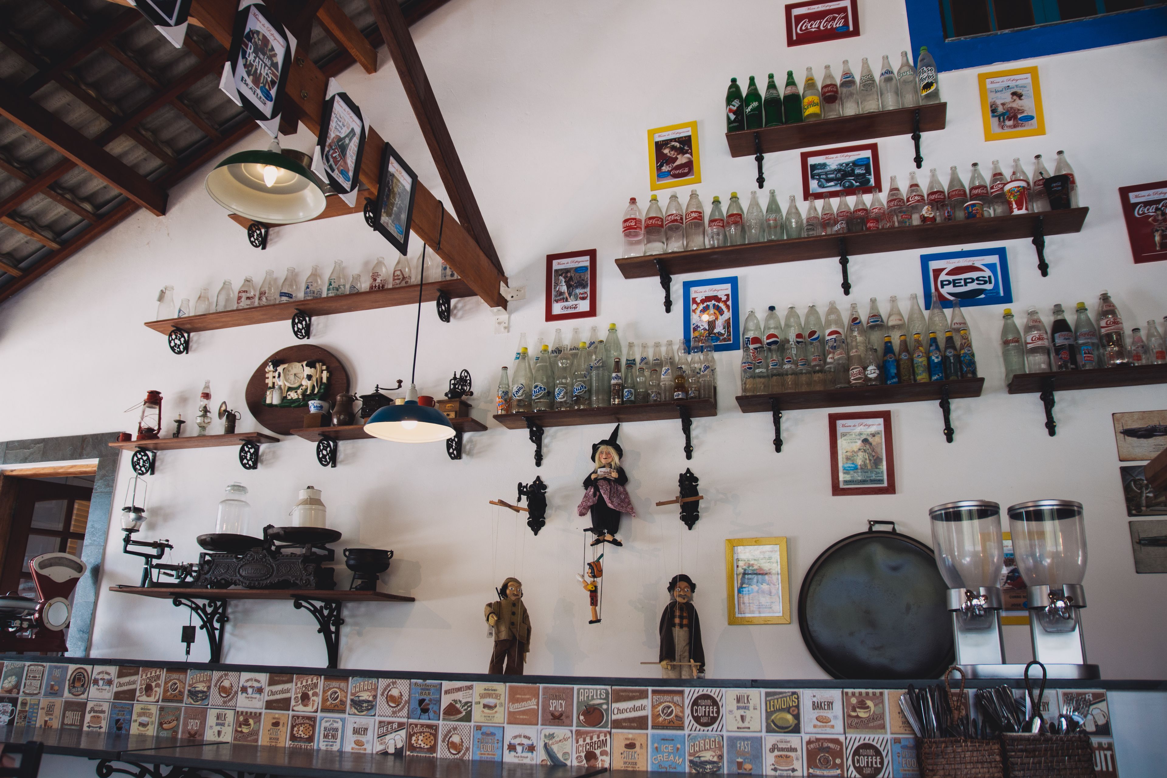 Un bar avec des étagères remplies de bouteilles de boissons, de vieux appareils à café et divers affiches accrochées au mur.