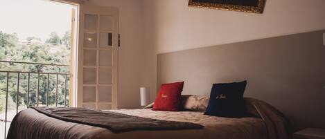 A bedroom with a bed, a window, a door, and a framed picture on the wall.