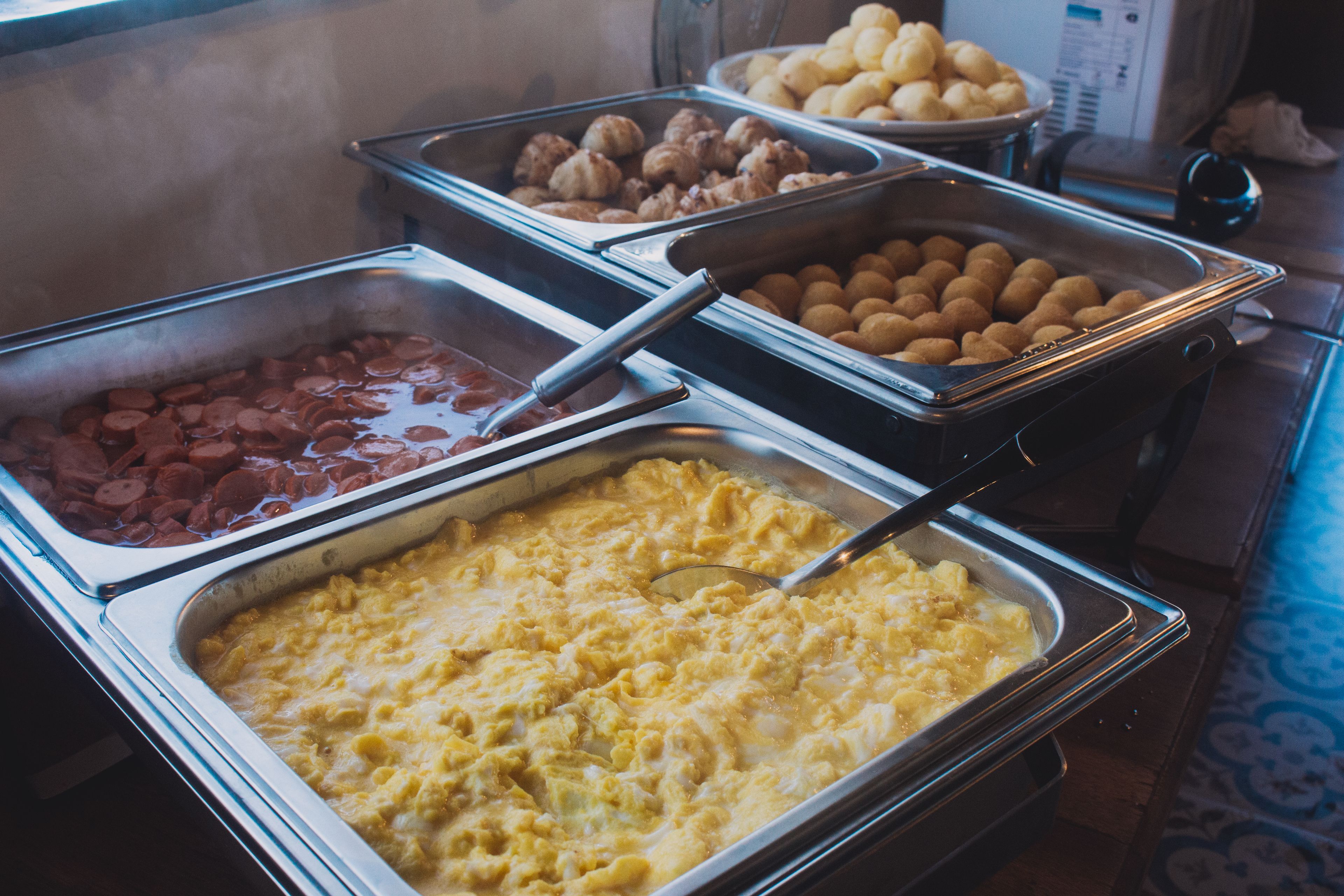 A buffet with various food options including scrambled eggs, sausages, and pastries.
