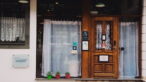 A hotel entrance with a wooden door, a sign for 'MUSE DO REFRIGERANTE', and a 'VIP Lounge' sign. There are three potted plants on the ledge. - Hotel Casarão da Ducha (Campos do Jordão)