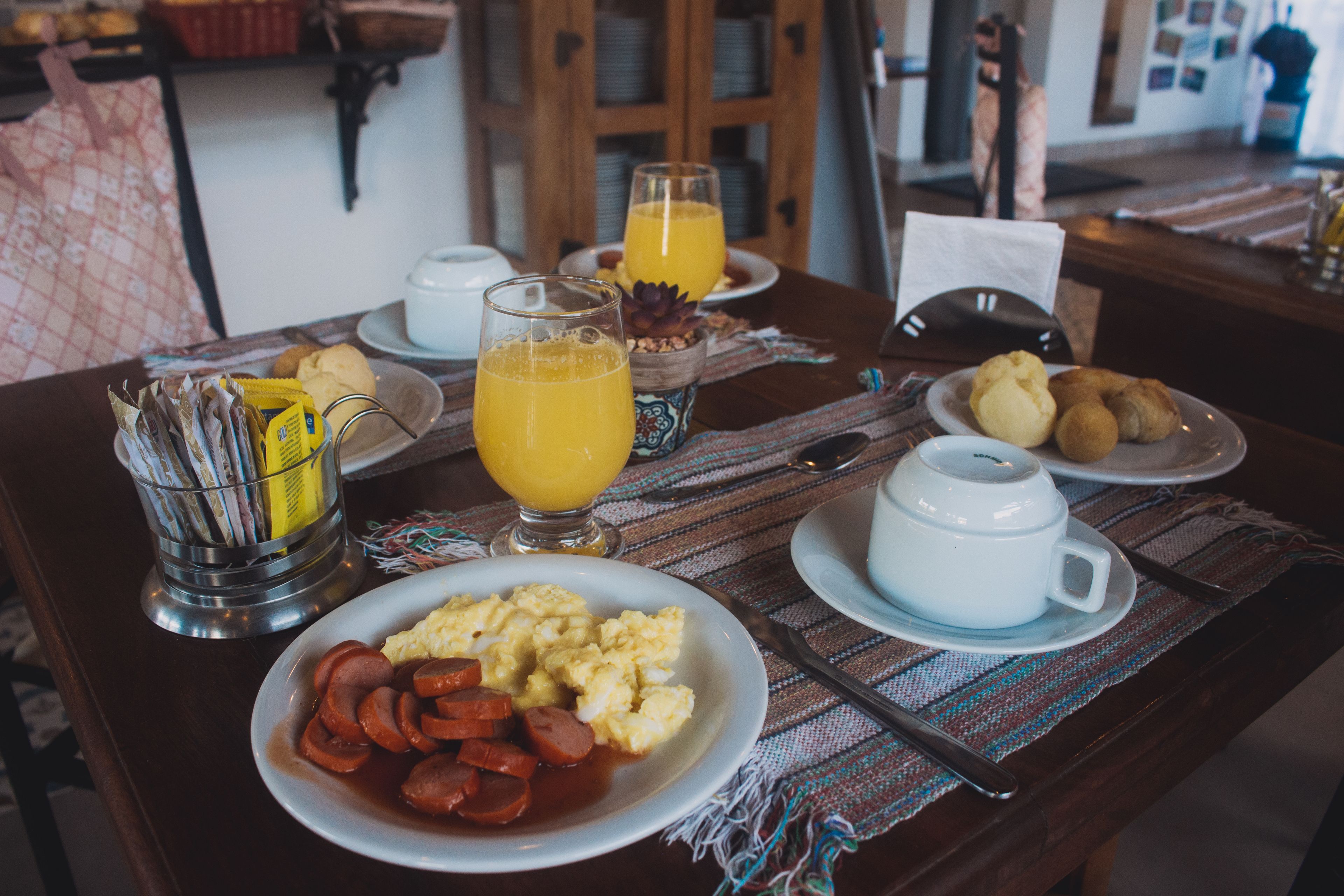 Una mesa de desayuno con platos de comida, vasos de jugo de naranja y una cafetera.