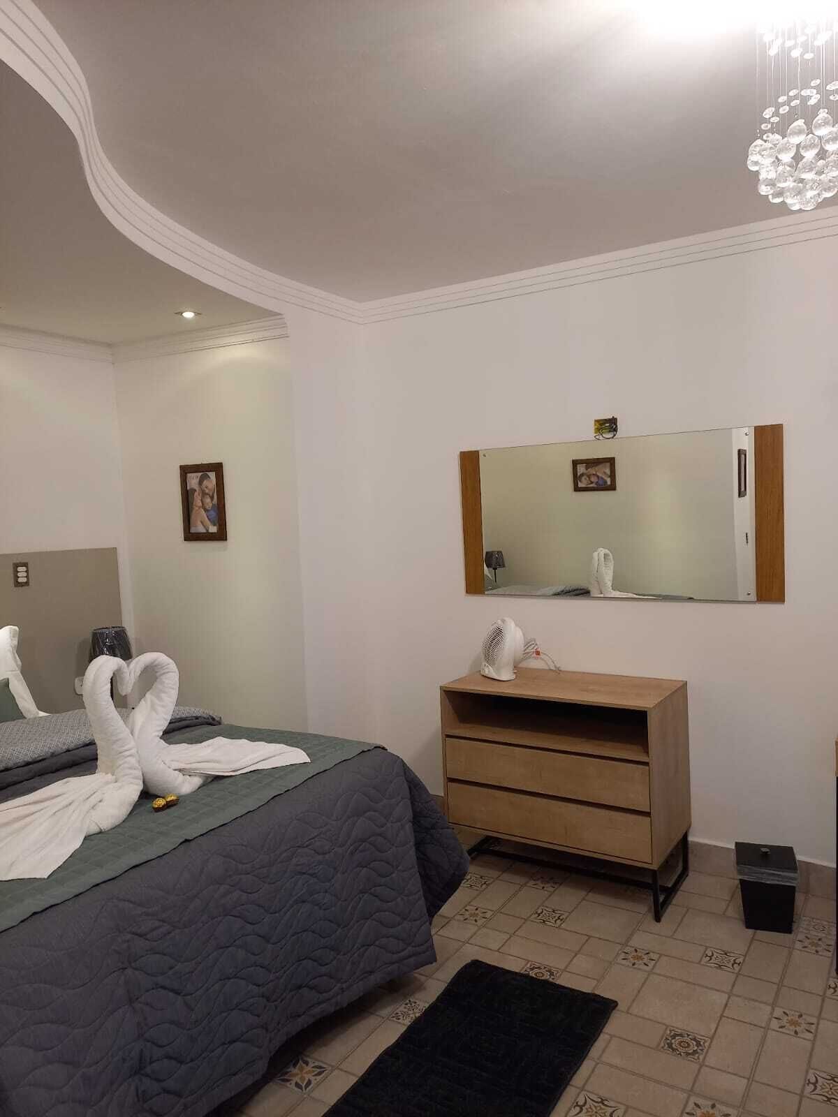 Una habitación de hotel con una cama, un tocador de madera, un espejo y una lámpara en el techo.