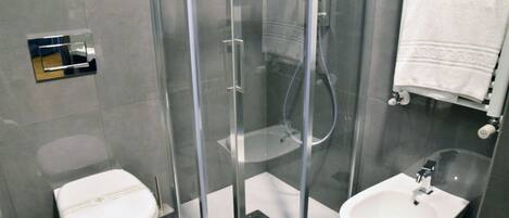 Un baño moderno con ducha de mampara de vidrio, inodoro y lavamanos.